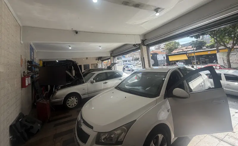 Oficina da Jovem Guarda por dentro, com carros em atendimento e um capô aberto